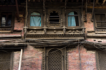 Old building in the city of Kathmandu, traditional Newari wood carvings in Nepal, ancient construction, no glass windows with blue curtains, dusty pollution, red brick design