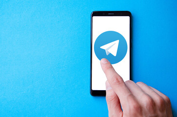 A male hand holds a smartphone, points a finger, types. Communication on a smartphone, correspondence. Place for text. Smartphone in hand on a blue  background.