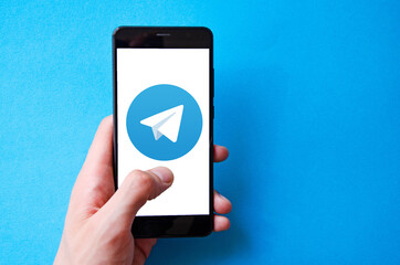 A male hand holds a smartphone, points a finger, types. Communication on a smartphone, correspondence. Place for text. Smartphone in hand on a blue  background.