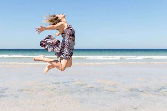 Middle-aged blonde woman in a green dress jumping on the beach