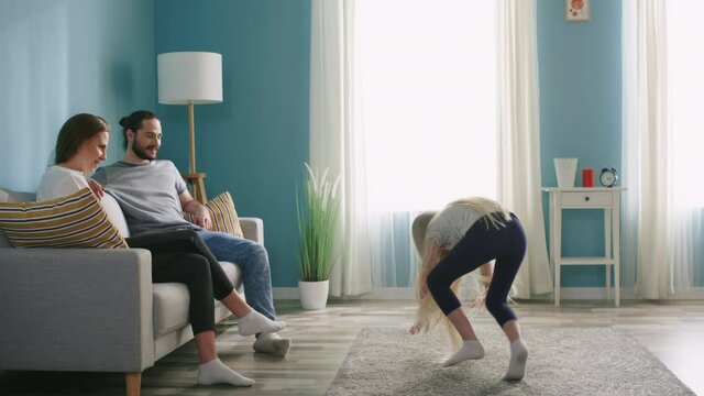 Small pretty blonde girl is playing pantomime with her parents, showing elephant with gestures, making funny faces, all have great weekend together, happy family life, Slow motion.