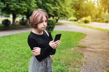 A young sad teenage girl looks at the phone and reads a message from a friend who promised to come to the meeting and did not come. Sad girl with a phone in her hands