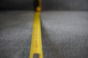 Closeup shot of a yellow measuring tape on the gray carpet