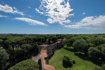 Fototapeta na wymiar Skyline of the city of Rome and the Aurelian walls of the Roman age. This stretch is at the main entrance of Porta San Sebastiano and is part of the Appia Antica regional park. Sun with clouds. Italy.