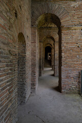 Perspective view of the walkway inside the Aurelian Walls of Rome at Porta San Sebastiano. Support arches in brick and cobblestone floor. At the end of the path there is a small glow of light. Italy