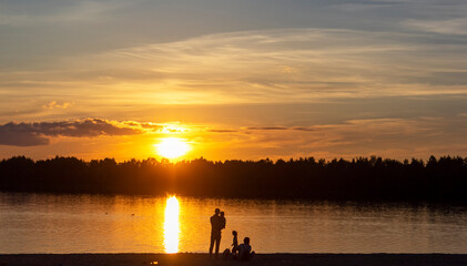 Naklejka na ściany i meble Beautiful sunset in the summer heat on the lake. Family silhouettes on the shore
