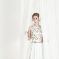 Shot of beautiful girl in long white dress hiding behind a white cloth. Portrait of beautiful young bride in beautiful white dress. Bride concept.