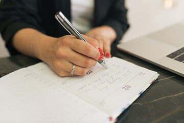 Naklejka premium woman's hand with red nails writing with a grey pen in the diary 