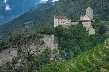 Fototapeta na wymiar View of Tirolo medieval castle above Merano, built on top a rocky mountain terrace, as seen from the Apple Orchards trail above the town, Merano, South Tirol, Italy.