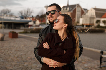 Fototapeta premium Caring For Your Love Concept. Close-up toned photo of happy fashionable couple in lone in sunglasses hugging each other. Man hugs her beloved woman wife. Urban photo style. Romantic date.