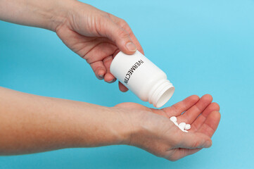 Treatments for Coronavirus (COVID-19): Ivermectin - White plastic packaging bottle in the hands with tablets. Isolated on blue background. Horizontal shot.
