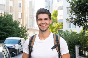 Portrait of a young handsome man with a big smile and a backpack in the urban city 