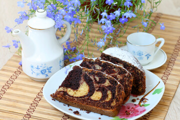 beautiful pieces of delicious chocolate cake sprinkled with powdered sugar on the background of a tea set and a flower