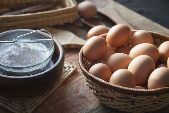 Closeup of eggs in a basket next to a bowl filled with flour on a wooden table