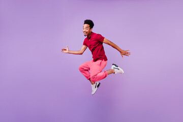 Fototapeta na wymiar Blithesome black brunette man dancing with happy smile. Indoor photo of inspired guy in red pants and white shoes jumping in studio.