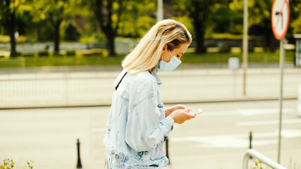 Young woman wearing antibacterial mask using phone in a city.