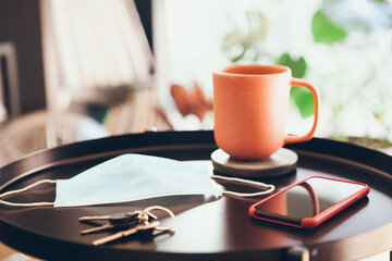 New normality. Staying home after work day, resting and taking off the surgical mask. Self distancing. Close-up of coffee table with cup of tea and face mask. Selective focus.