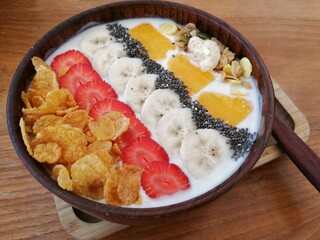 A bowl of flakes, grains, pecans, yogurt, oat, sliced strawberries and bananas