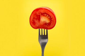 Half a red fresh tomato on a fork on a yellow background