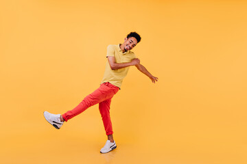 Blithesome african boy dancing on yellow background. Well-dressed male model with black hair expressing happiness.