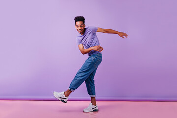 Full-length photo of glad african man dancing with sincere smile. Male model in jeans and purple...