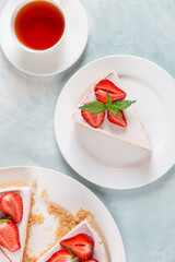 Sweet breakfast, tea and delicious cheesecake with fresh strawberries and mint, homemade recipe without baking, on a blue stone table. Copy space.