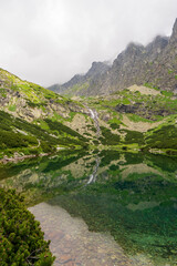 Scenic view of foggy mountains cover by dark clouds and green forest with a reflection in a lake. Stony shore. velicke pleso. Velicke lake. High Tatras,  Slovakia Concept of nature and tourism