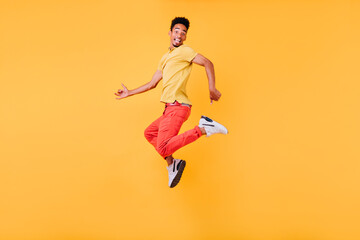 Fototapeta na wymiar Amazed black male model fooling around on yellow background. Refined short-haired african guy jumping in studio.