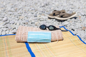 protective medical mask, beach towel, swimming goggles and men's flip-flops on the beach. Concept...
