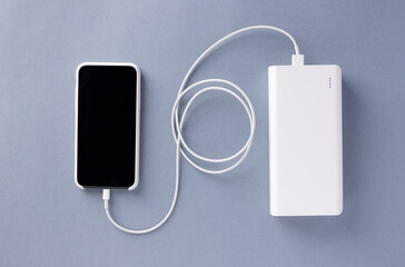 smartphone in a white case is charged from a white Power bank charger. Modern technology. blue...