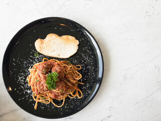 Pork spaghetti, sprinkled with cheese around and with parsley and bread on a black plate and soft white background. There is a copy space on the right.