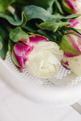 Pink parrot tulips with green stems and leaves lying in a white net metal basket