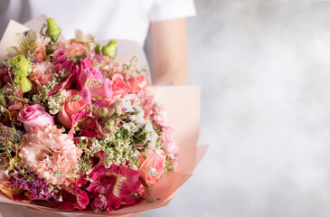 Obraz na płótnie Canvas Beautiful bouquet of mixed flowers in female hands. roses, eustomas, alstroemerias. beautiful gift for your beloved woman. place for text. Gray background