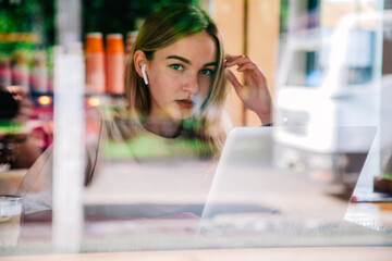 Girl in coffee shop window works on laptop sipping cappuccino