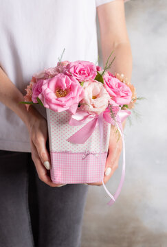 young woman holding a flower box with delicate pink roses and eustomas. blooming gift for a woman. vertical image. Gray background