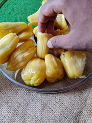 Indian man picking up jackfruit in a glass plate on sack background.