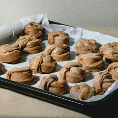 Ready to bake traditional Swedish cinnamon sweet buns Kanelbulle on oven tray cover by baking paper on grey linen table cloth.