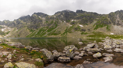 Scenic view of mountains clouds and green with a reflection in a frogs lake. Stony shore. hlincovo pleso. hlincovo lake. High Tatras, Slovakia Concept of nature and tourism