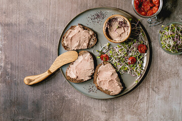 Sandwiches and ceramic bowl of homemade chicken liver pate with wooden knife, sun-dried tomatoes...