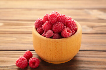 Ripe raspberries in wooden bowl on brown background. Top view