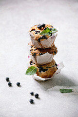 Homemade blueberry muffins in paper cupcake holder in stack decorated by fresh berries and mint leaves on light grey background.