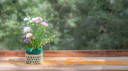 Flowers in a basket placed on a wooden table with natural sunlight spreading thin and copy space.