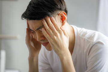 Young Asian man is worried and headache as he is quarantined to the house during the outbreak of...