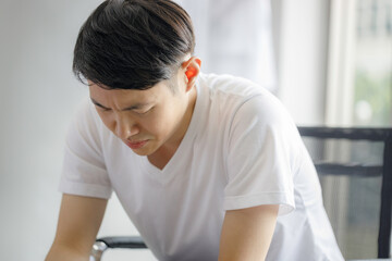 Young Asian man is worried and headache as he is quarantined to the house during the outbreak of...