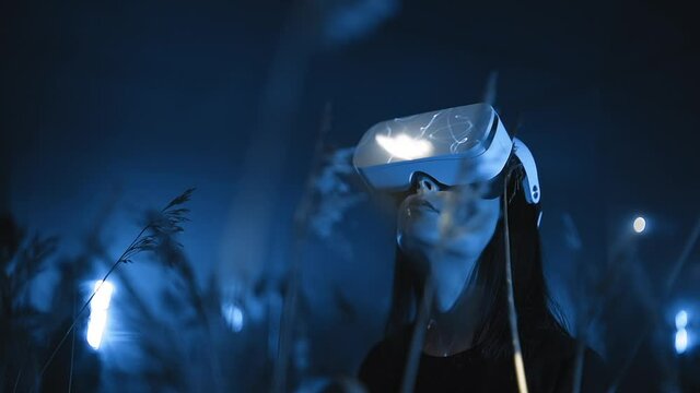 portrait of girl in VR headset or glasses looking around at night in nature in forest or field, modern technologies of virtual or augmented reality 3D graphics and holographic projection
