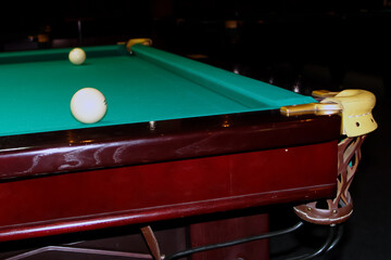  two billiard balls on a green pool table, a pocket in the corner of the table