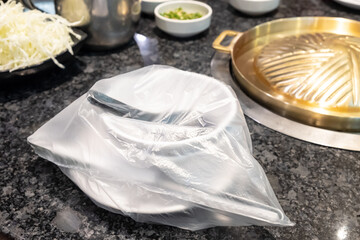 Spoon and dish cover by a plastic at Japanese barbecue grill restaurant. New normal lifestyle that need to sanitize utensil before use. Coronavirus pandemic effect.