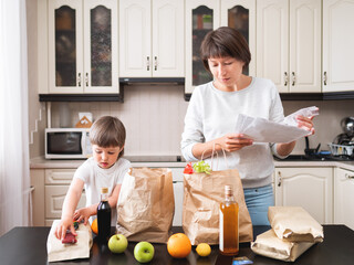 Woman and toddler boys sorts out purchases in the kitchen. Grocery delivery in paper bags....
