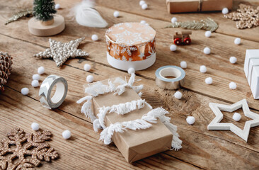 Christmas presents wrapped in craft paper with white fluffy pompons and fringe as decoration. Wooden table with hand hand made New Year gifts.