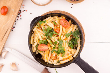Fast and simple Italian pasta with tomatoes and garlic sprinkled with parsley in a frying pan on a light table with cooking ingredients, top view